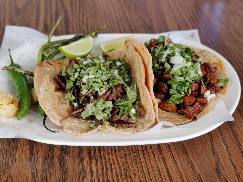 Three street tacos with cilantro, onion and lime on a plate