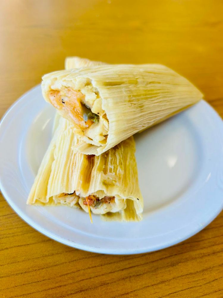 Two homemade tamales in corn husks on a white plate